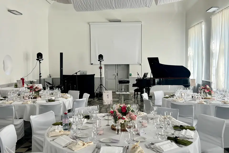 Salle de réception dressée avec un piano à queue, la cabine DJ et l’éclairage
